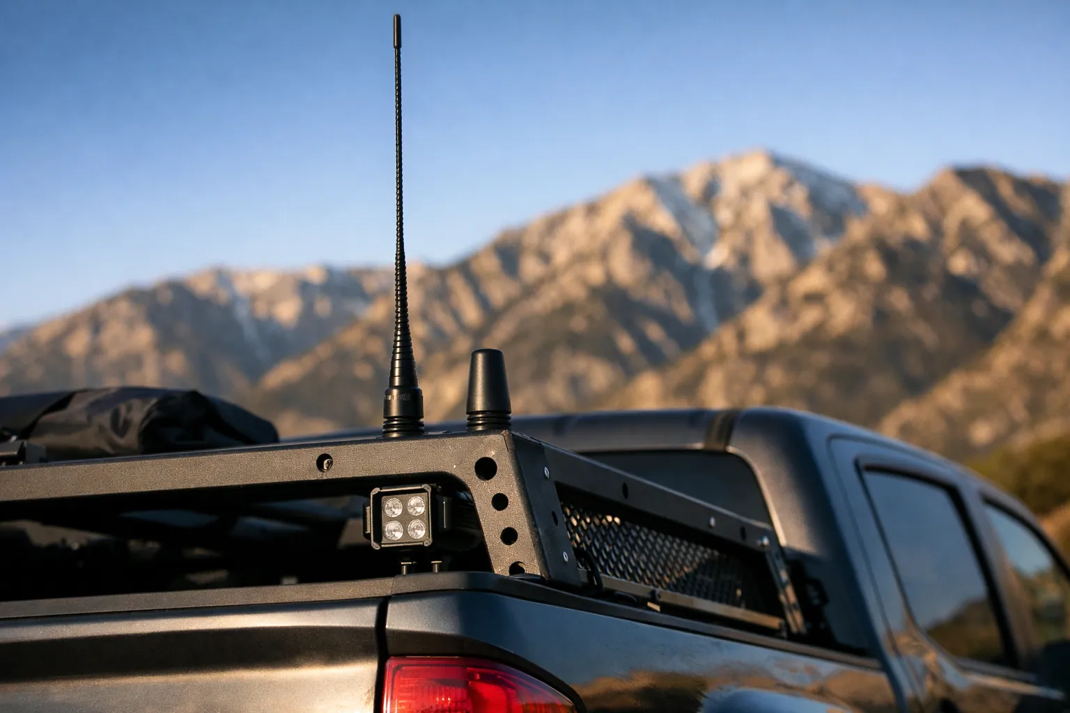 A tall whip antenna next to a short stubby antenna on a truck bed rack